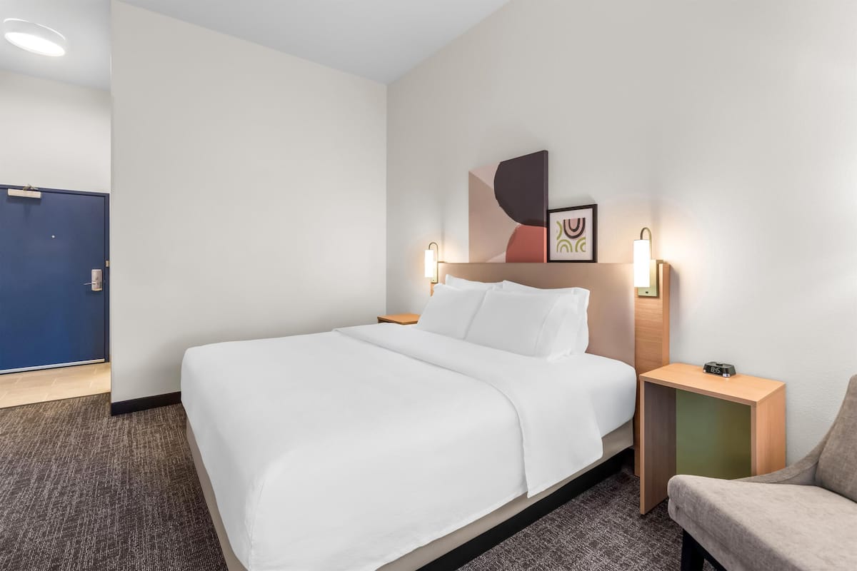 Una habitación de hotel con una cama, una mesita de noche, una silla y una puerta.