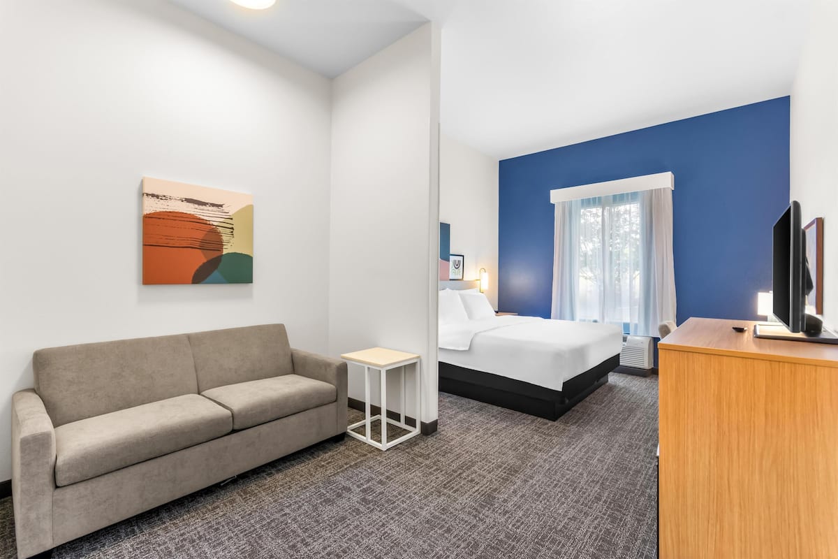 Habitación de hotel con sofá, una mesita, cama, televisión y un cuadro en la pared.