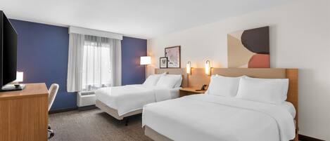 A hotel room with two beds, a desk, a TV, and a window with curtains.