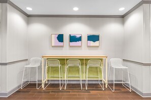 A room with a white wall, three framed artworks, a wooden counter, and four white chairs. - Spark by Hilton Dothan (Dothan)