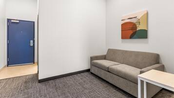 Una habitación con una puerta azul, un sofá color beige, una mesita blanca pequeña y un cuadro abstracto de colores en la pared.