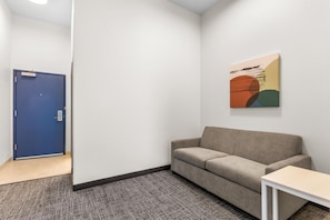A room with a blue door, a beige sofa, a small white table, and a colorful abstract painting on the wall. - Spark by Hilton Dothan (Dothan)