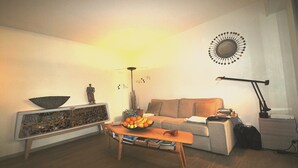 Un soggiorno con tavolino in legno, divano, credenza con oggetti decorativi, uno specchio appeso al muro e una lampada da terra.