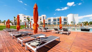 Un resort con terraza de madera, sillas de descanso y sombrillas naranjas.
