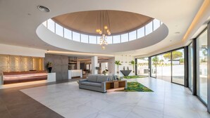 Un vestíbulo espacioso con techo curvo, una mesa de recepción, un área de estar con sofá y amplias ventanas que ofrecen vistas al exterior.