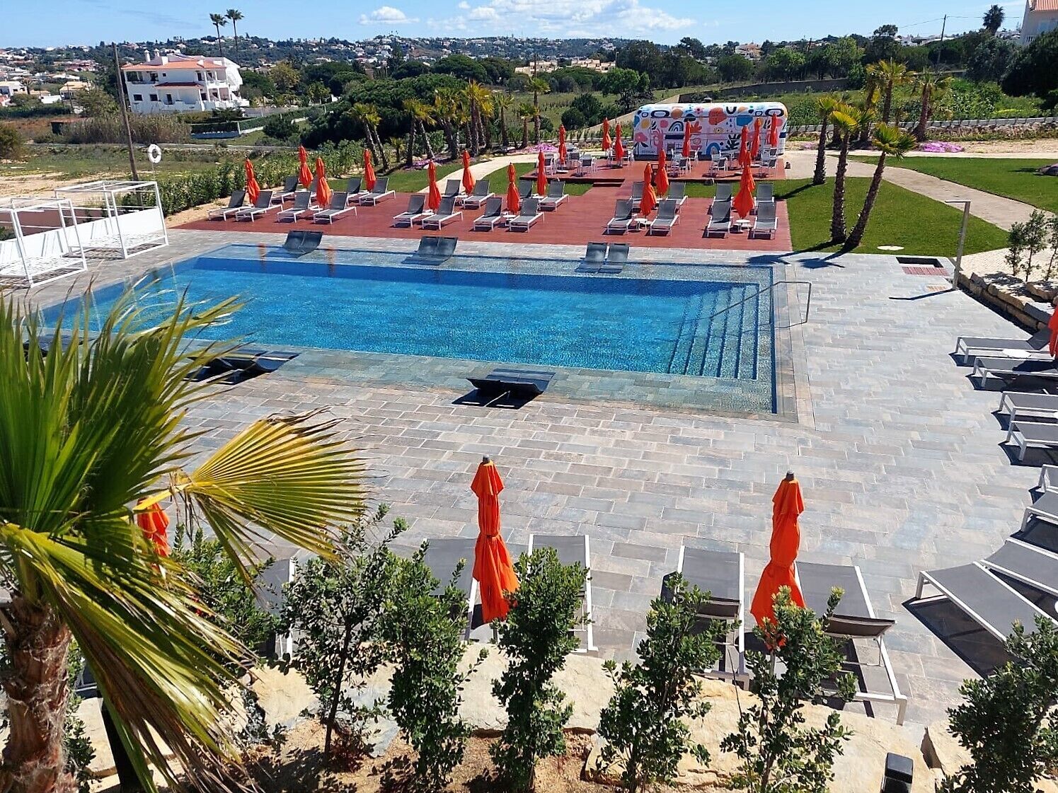 Une piscine dotée de chaises longues et de parasols, entourée de palmiers et offrant une vue sur une colline.