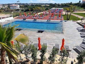 Una piscina con tumbonas y sombrillas, rodeada de palmeras y vistas a una colina.