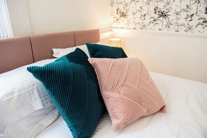 Ein Bett mit Kopfteil, Kissen und einer Wand mit Blumenmuster.