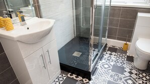 Un baño con lavamanos blanco, cabina de ducha de vidrio y baldosas de suelo estampadas.