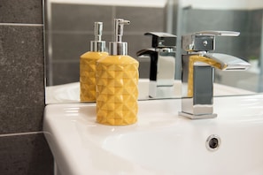 A bathroom with a white sink, a chrome faucet, and two yellow soap dispensers.