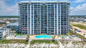 Un hotel de gran altura con múltiples balcones, una piscina central y ubicación frente a la playa.