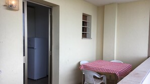 A small room with a table and chairs, a refrigerator, a window with shelves, and a door leading to another room. - [lido Adriano] Appartamento con Vista Mare (lido adriano)