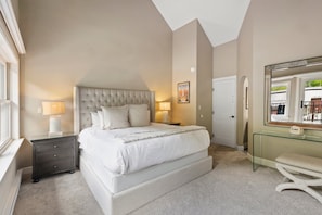 A bedroom with a large bed, bedside lamps, a glass console table, and a mirror.
