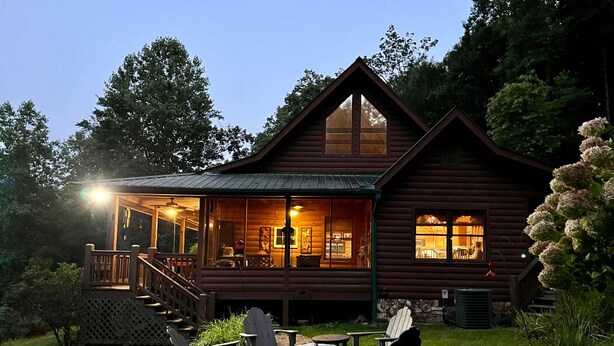 A log cabin with a porch, outdoor seating, and a well-lit interior. - Rocky Top Retreat  Hot Tub & Mountain Views (Suches)