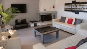 Un salon moderne avec un canapé blanc, une table basse en verre, une cheminée et un téléviseur fixé au mur.