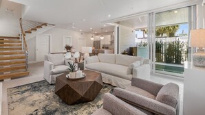 A modern living room with a staircase, a dining area, and a kitchen.