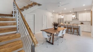 A modern kitchen with white cabinets, a wooden dining table, and a staircase with wooden steps and metal railings.