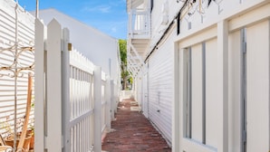 A narrow brick pathway flanked by white buildings with balconies and windows.