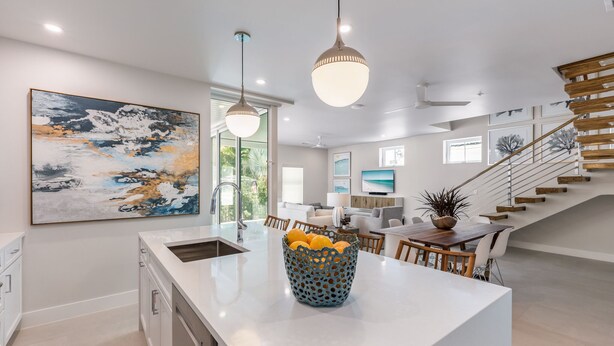 A modern kitchen with a large island, pendant lights, and a staircase leading to a loft area.