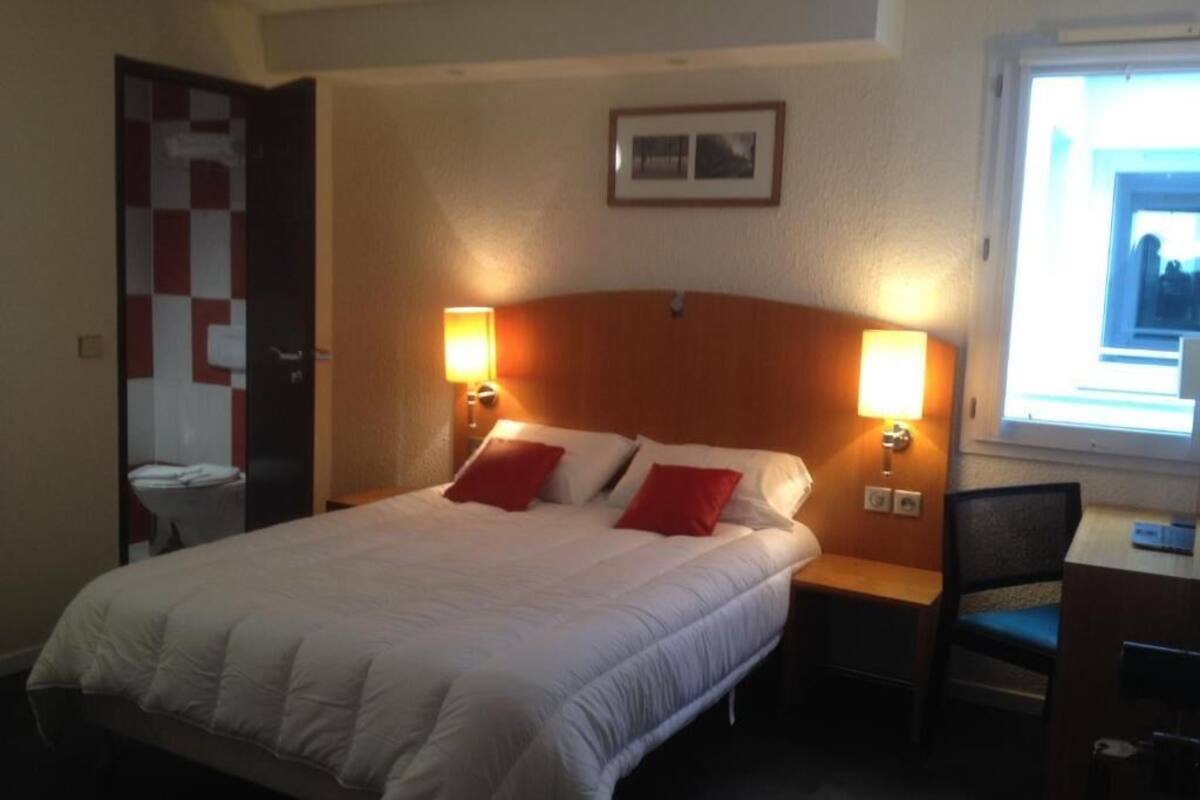 A hotel room with a large bed, two bedside lamps, a desk, and a chair.