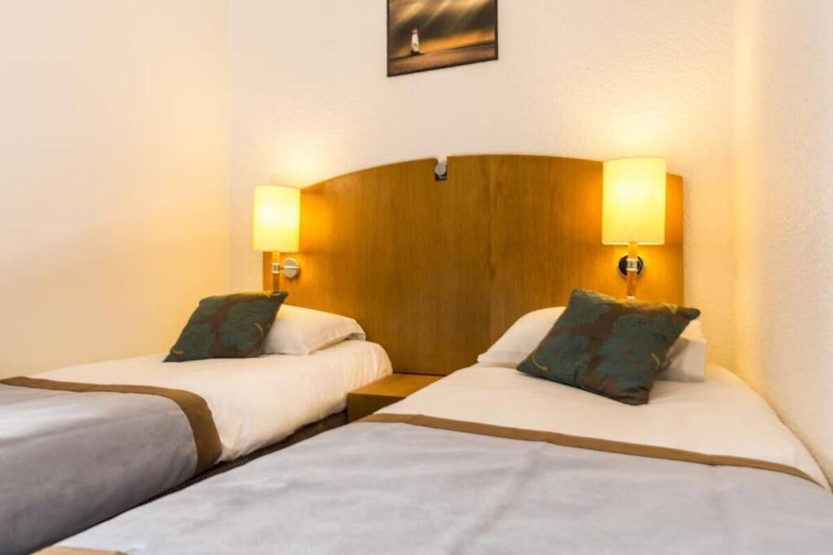A hotel room with two single beds, each with a wooden headboard and bedside lamps.