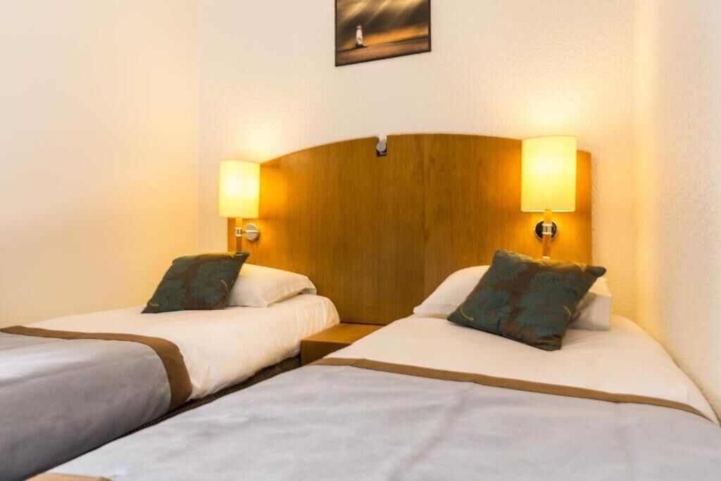 Una camera d'albergo con due letti singoli, ognuno dotato di una testiera in legno e lampade da comodino.