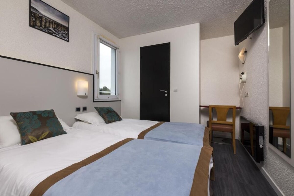 Une chambre d’hôtel avec deux lits, un bureau, une chaise, une télévision et une fenêtre.