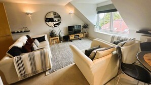 Een moderne woonkamer met een hoge plafond, een groot raam en een gezellige zithoek met een bank en fauteuils.