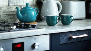 A kitchen with a stove, a kettle, and two cups on the counter.