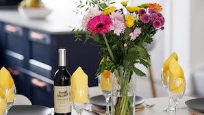 A dining table set with plates, cutlery, a bottle of wine, and a vase of flowers.