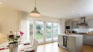 A modern kitchen with a central island, a dining area with a table set for two, and a large sliding glass door leading to a garden.