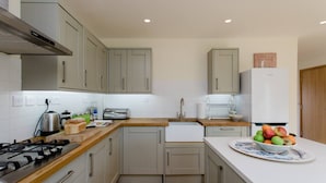 A modern kitchen with grey cabinets, a wooden countertop, a gas stove, a sink, and a refrigerator.