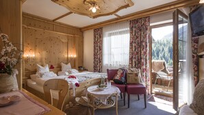 A cozy hotel room with a wooden ceiling, a bed with white linens, a small round table with a pitcher, a chair, and a sofa. - Landhaus Dengg in Gerlos, "Almliebe" Apartment for 2 to 3 people (Gerlos)