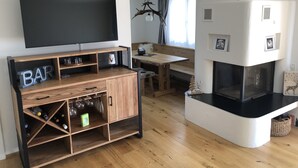 A modern living room with a wooden entertainment unit, a flat-screen TV, a fireplace, and a dining area with a bench and table. - Renovated 3 Rooms Apartment in Ruschein Near Laax (Ilanz)