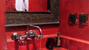 Une salle de bain avec un lavabo aux carreaux rouges, un robinet de style rétro, un miroir aux motifs décoratifs et un petit récipient noir.