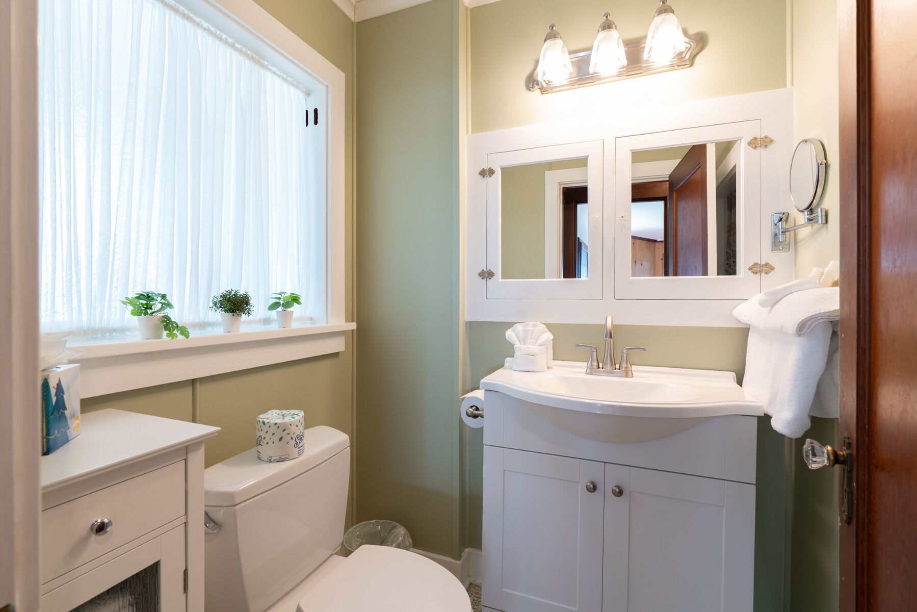 Ein Badezimmer mit Toilette, Waschbecken und Fenster mit Pflanzen.
