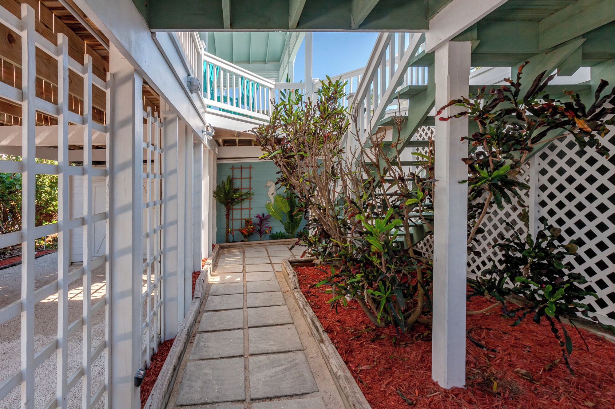A covered walkway with a tiled floor, surrounded by plants and a white lattice fence.