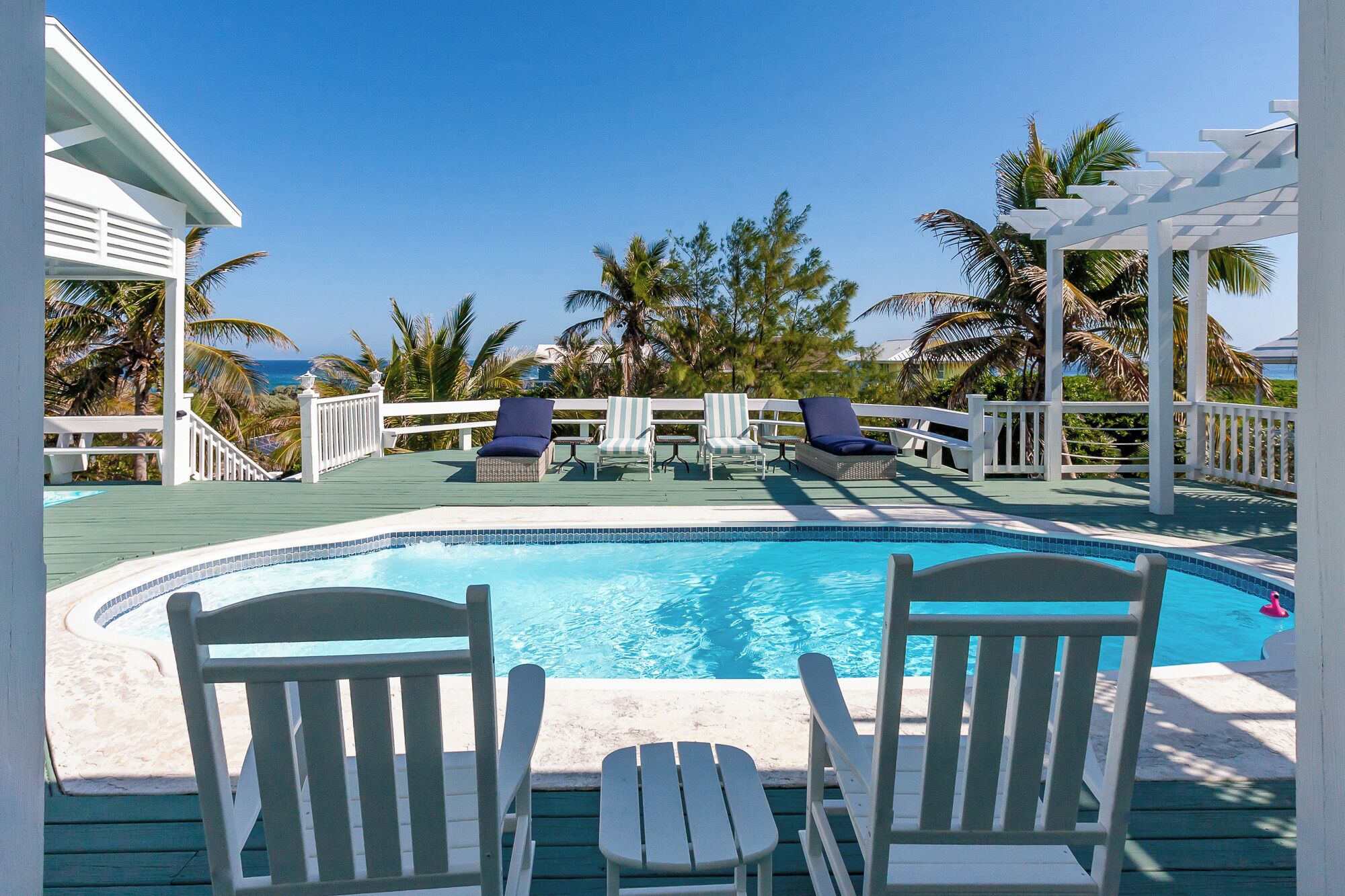 A pool area with a clear view of the ocean, surrounded by palm trees and white railings.