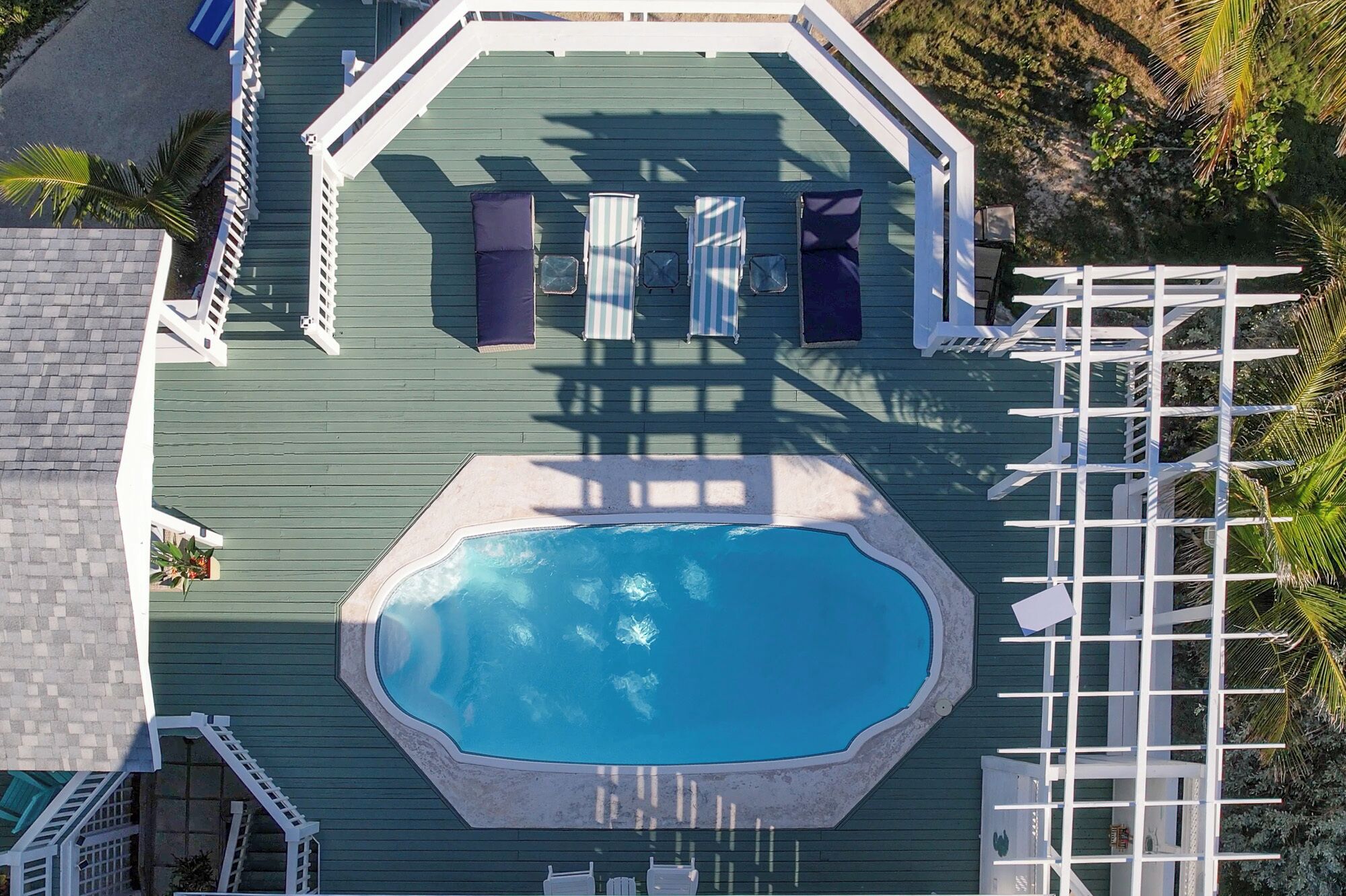 An octagonal swimming pool with a surrounding deck, a white fence, and lounge chairs.