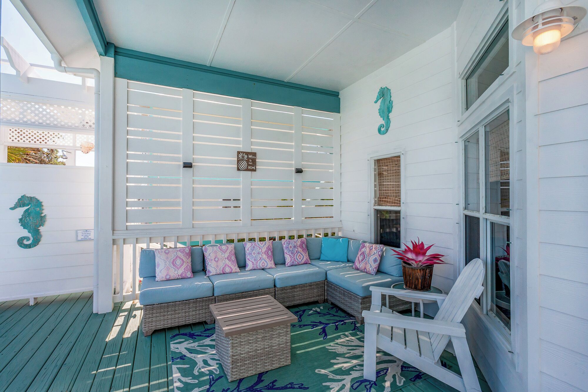 A covered porch with a blue and white color scheme, featuring a cushioned seating area with patterned cushions, a wicker coffee table, and a potted plant.