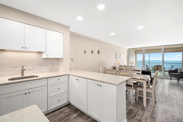 A modern kitchen with white cabinetry, a wooden dining area, and a balcony with a view of the ocean. - English Towers-Beautiful Direct Ocean Views from this Remodeled Condo! (Ocean City)