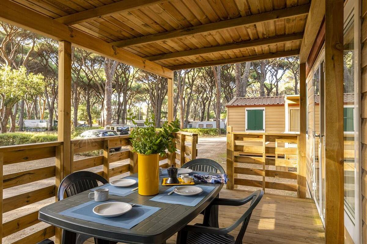 Un área de comedor al aire libre techada, con una mesa lista para dos personas, rodeada de barandas de madera y sillas.