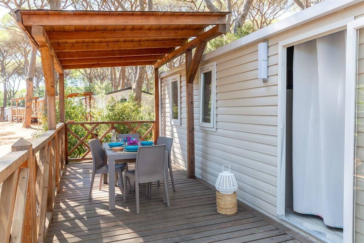 Una terraza de madera con una mesa y sillas, una zona cubierta y un edificio de estilo cabaña.