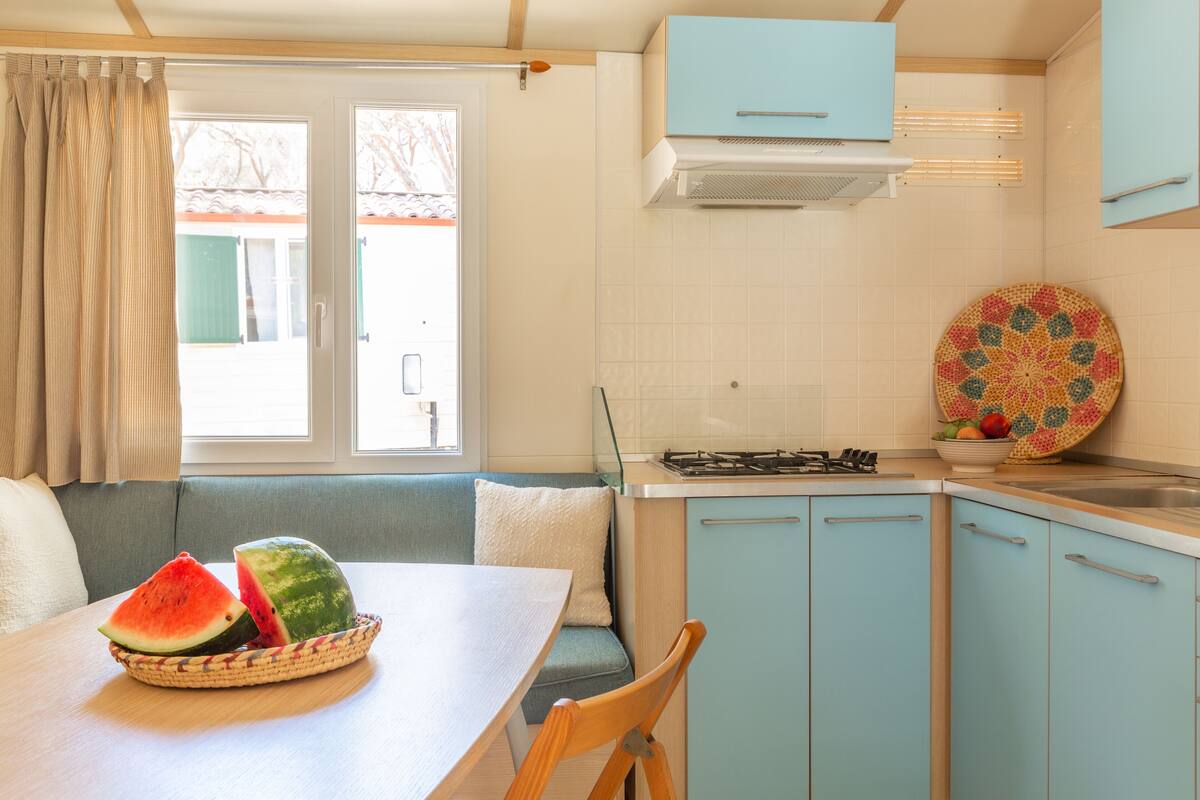 Cocina compacta con comedor, que incluye estufa, armarios y una ventana con cortinas.