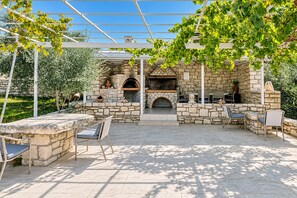 An outdoor patio with stone walls, a built-in grill, and seating areas. - Villa Avra - With Private Pool (Rethymno)
