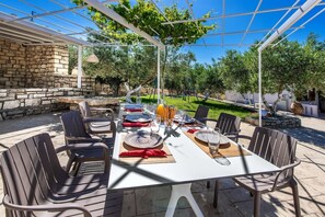 An outdoor dining area with a stone wall, a pergola, and a table set for four with chairs.