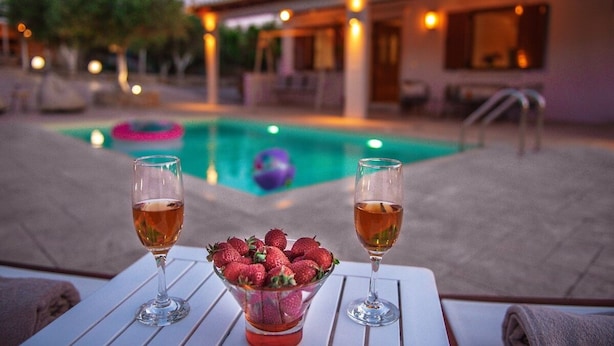 Cenário à beira da piscina com dois copos de vinho e uma taça de morangos sobre uma mesa branca.