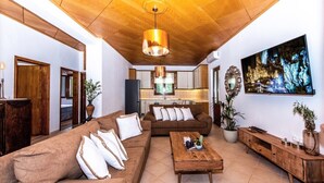Uma sala de estar espaçosa com teto de madeira, uma grande TV de tela plana e um conjunto de sofá aconchegante.