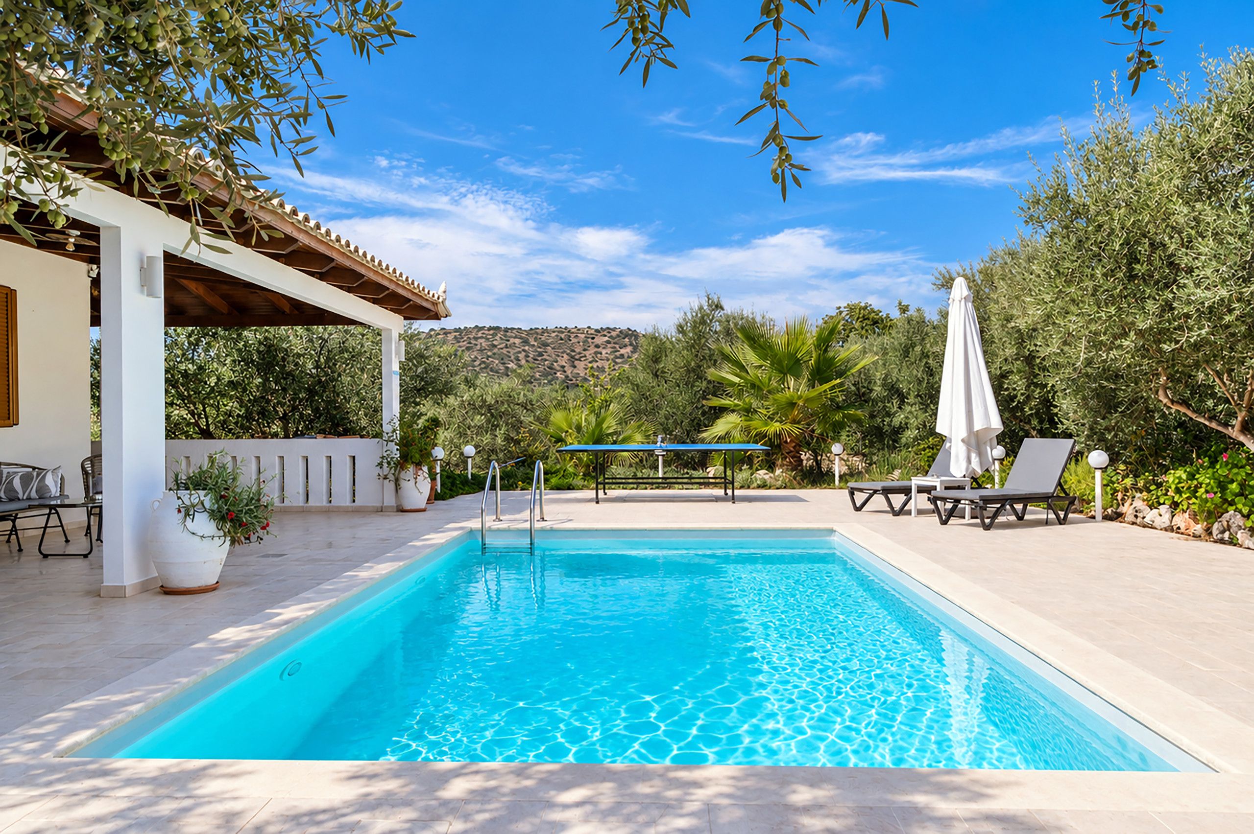 A swimming pool with a pergola, lounge chairs, and a view of a hilly landscape.