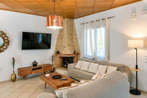 A living room with a fireplace, a sofa, a coffee table, a TV, and a lamp. - Villa Avra - With Private Pool (Rethymno)